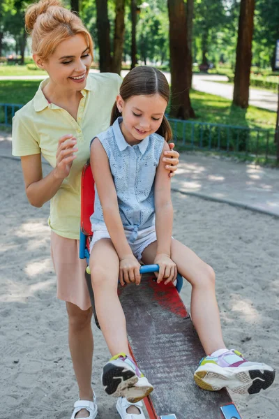 Kvinna Leende Nära Dotter Ridning Gungbräda Lekplatsen — Stockfoto