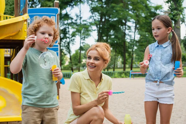 Menino Soprando Bolha Sabão Perto Sorrindo Mãe Irmã Playground — Fotografia de Stock