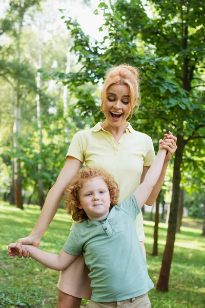 一个兴奋的女人牵着儿子的手在夏天的公园里玩乐 — 图库照片