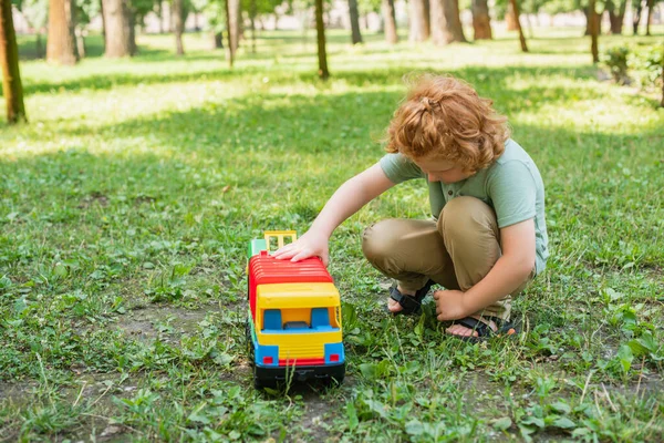 緑の芝生の上でおもちゃのトラックで遊んでいる赤毛の男の子の完全な長さビュー — ストック写真