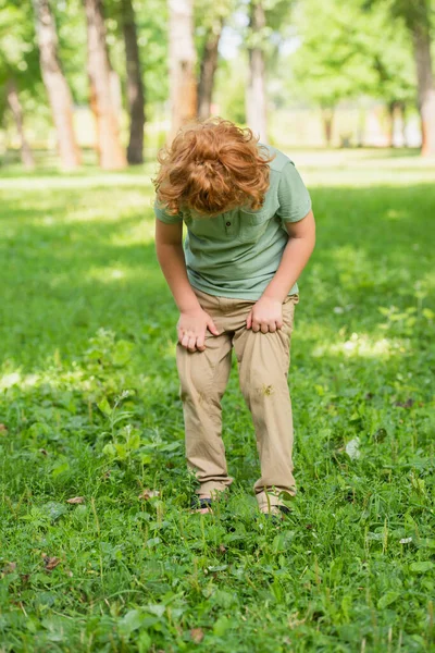 芝生の上に立って汚いズボンを見ている赤毛の少年の完全な長さのビュー — ストック写真