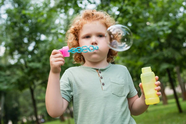 赤い頭の男の子が夏の公園でシャボン玉を吹いて — ストック写真