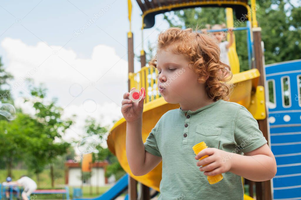 curly boy blowing soap bubbles on playground