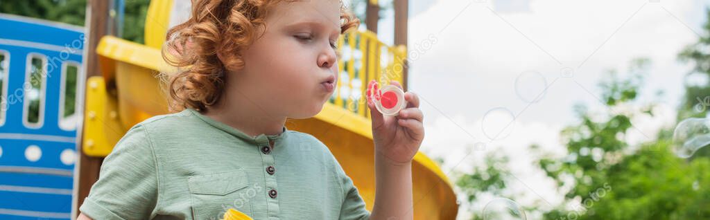 curly boy blowing soap bubbles while spending time outdoors, banner