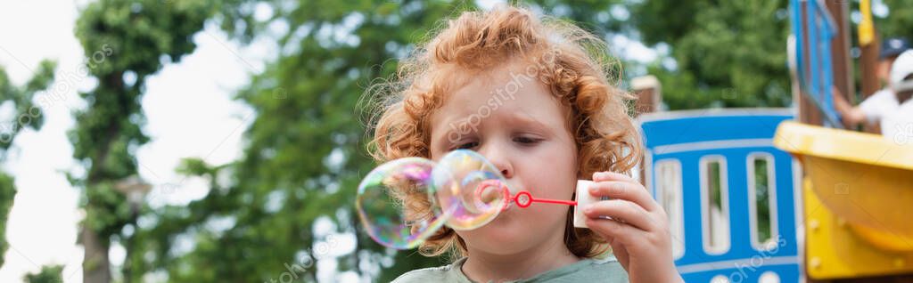 boy blowing soap bubbles outdoors in park, banner