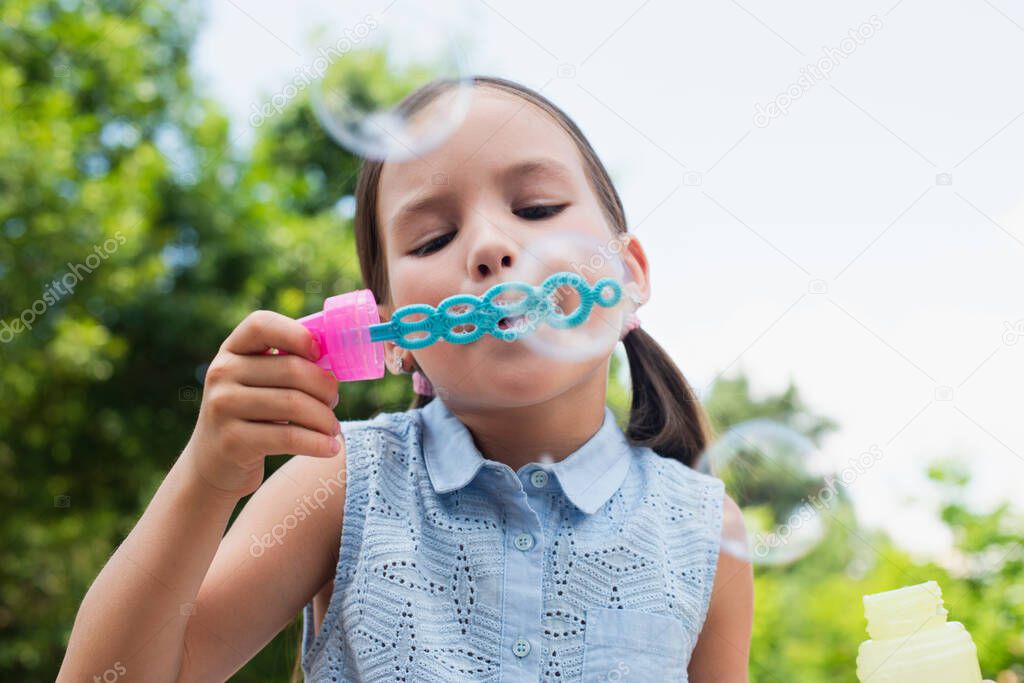 girl blowing soap bubbles on blurred foreground