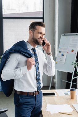 Bulanık ofiste akıllı telefonla konuşurken ceketi tutan mutlu ekonomist.