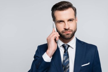 Esmer işadamı cep telefonundan arıyor ve gri kameraya bakıyor.