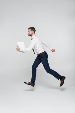 Beyaz gömlekli iş adamının yan görünüşü gri tabletle koşuyor