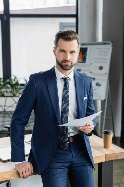 Ekonom Kostym Innehav Dokument Och Tittar Kamera Nära Arbetsplatsen — Stockfoto