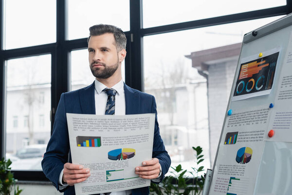 economist with infographics looking away near flipchart in office