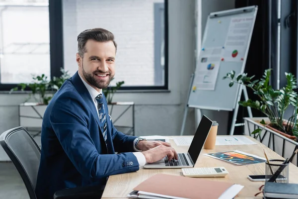 Happy Businessman Looking Camera While Typing Laptop Blank Screen — стоковое фото