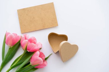 El işi kağıdının yanındaki pembe lalelerin ve beyaz üzerinde kalp şeklinde hediye paketlerinin üst görüntüsü.