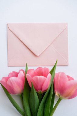 Pastel zarfın yanındaki pembe lalelerin beyaz üzerindeki üst görüntüsü.