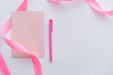 Kalemin yanındaki zarfın üst görüntüsü ve beyaz üzerine pembe kurdele
