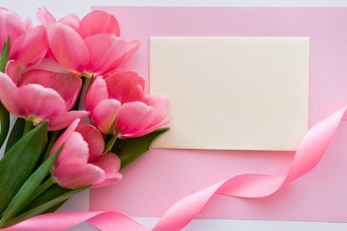 Kurdelenin yanında laleler ve beyaz ve pembe üzerine sarı zarf olan buket manzarası.