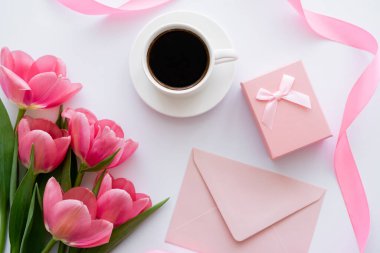 Kahve fincanının yanındaki lale buketi, hediye kutusu ve beyaz üzerine pembe zarf.
