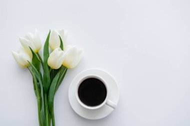 Bardağa yakın lalelerin üst görüntüsü, çay tabağında kahve, beyaz.