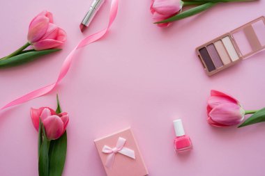 Dekoratif kozmetik ürünlerinin yanında fiyonklu hediye kutusu ve pembe lalelerin üst görünümü