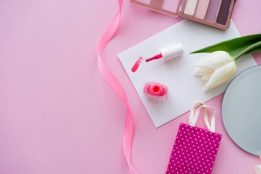 Lalenin yanındaki kartın üzerindeki ojenin fırça darbelerinin üst görüntüsü ve pembe üzerindeki göz farı paleti. 
