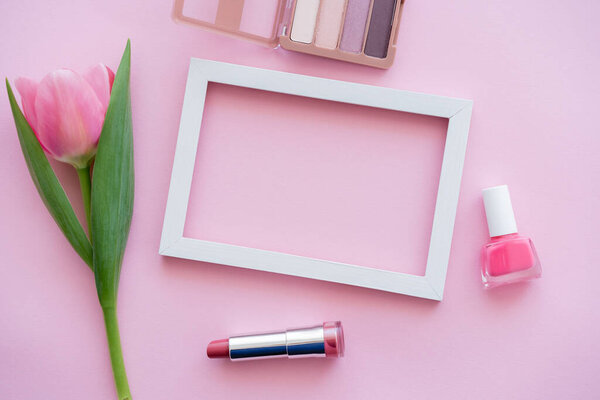 top view of decorative cosmetics near blooming tulip and frame on pink
