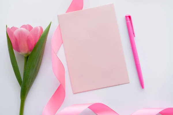 白色上粉红郁金香附近的彩带和信封的顶部视图 — 图库照片