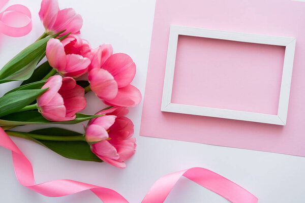 top view of bouquet with tulips near ribbon and frame on white and pink