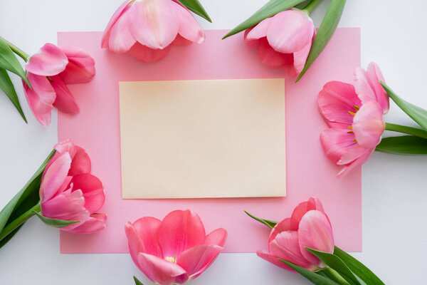 top view of frame with tulips near yellow envelope on white 