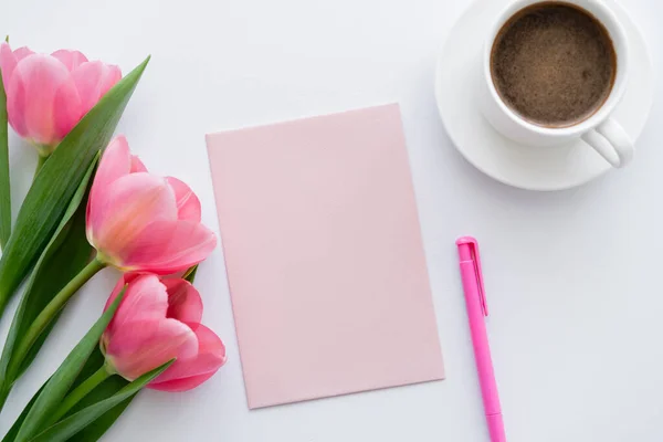 在粉红郁金香 白纸和白笔附近的一杯咖啡的顶部视图 — 图库照片