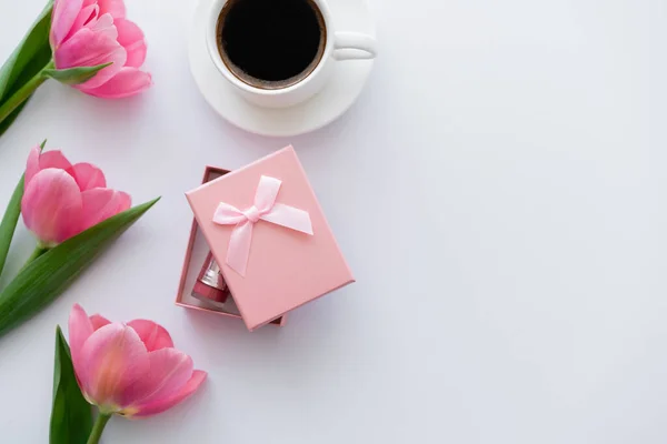 top view of cup of coffee near gift box and pink tulips on white