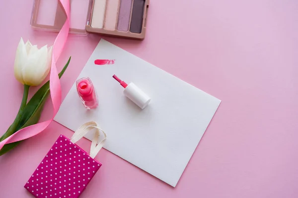 ネイルポリッシュ ホワイトチューリップ アイシャドウ ピンクの小さなショッピングバッグの近くの紙の上のブラシのビュー — ストック写真