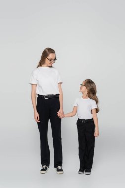 Anne ve çocuğun el ele tutuşup gri arka planda birbirlerine baktıkları uzun bir manzara.