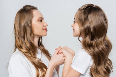 Kız ve kadının yan bakışları birbirine bakıyor ve gri renkte el ele tutuşuyorlar.