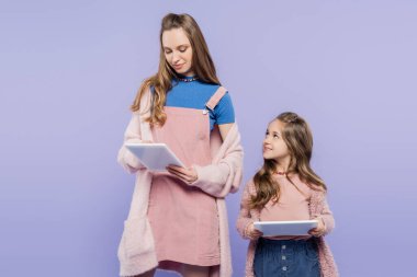 Elinde aletle gülümseyen bir çocuk ve mor üzerine izole edilmiş dijital tabletle annesine bakıyor. 