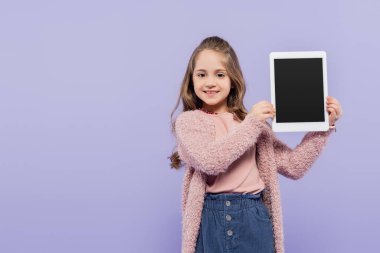 Mor üzerine izole edilmiş boş ekranlı dijital tablet tutan neşeli kız.