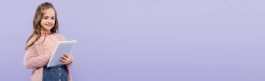 Mor ve pankartta izole edilmiş dijital tablet kullanan neşeli çocuk