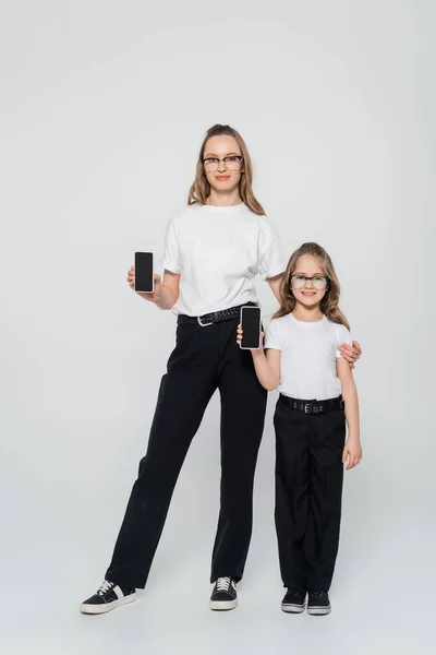 Full Length View Mother Daughter Eyeglasses Showing Smartphones Blank Screen — Stock Photo, Image