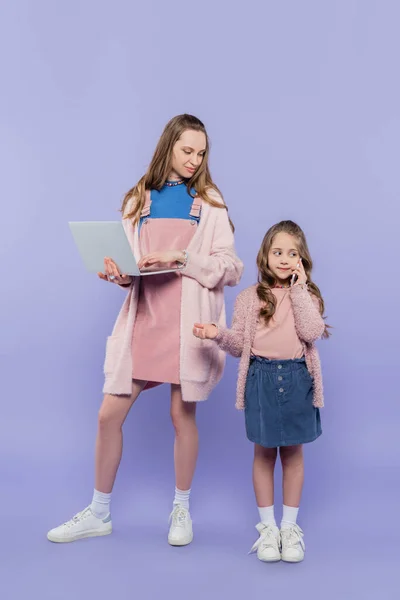 全长的母亲带着笔记本电脑 看着孩子们用紫色智能手机说话 — 图库照片