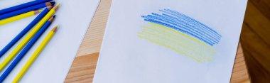top view of color pencils near white paper with blue and yellow strokes, banner clipart
