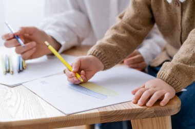 cropped view of patriotic child drawing ukrainian flag near blurred mother clipart