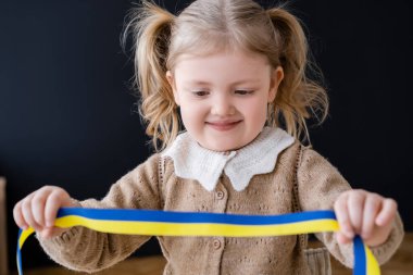 happy girl with ponytails holding blue and yellow ribbon on black clipart