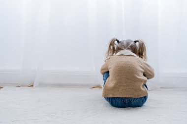 back view of upset child sitting on floor near white curtain clipart