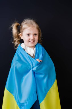 Ukrayna bayrağıyla kaplanmış mutlu bir kız siyah kameraya bakıyor.