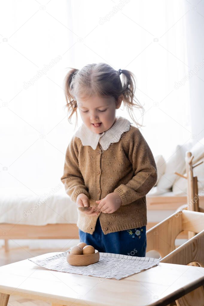 girl sticking out tongue while holdings spoon near bowl with wooden balls
