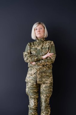 Siyahların üzerinde kollarını çapraz yapmış, kamuflajlı ciddi bir kadın.