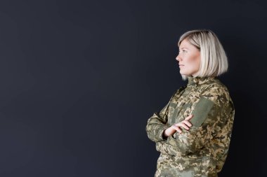 side view of woman in military uniform standing with crossed arms isolated on black clipart
