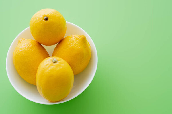 Top view of bright lemons in bowl on green background