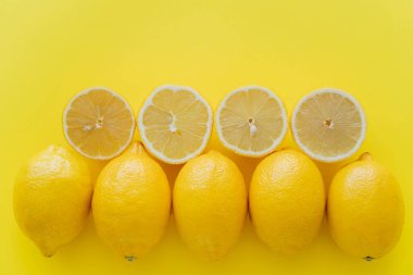 Top view of rows of whole and cut lemons on yellow surface  clipart