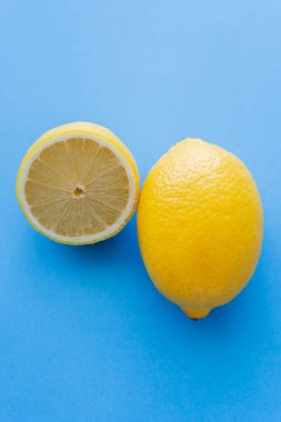 Close up view of cut and whole bright lemons on blue background