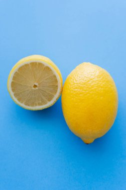 Close up view of cut and whole bright lemons on blue background clipart